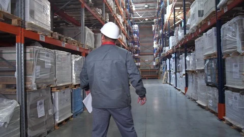 Warehouse worker goes back to the camera between the racks with the goods. 4K Stock Footage 111767135