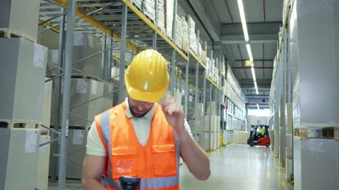 Warehouse worker in hard hat and safety vest navigates the aisles. Vidéo 307996315