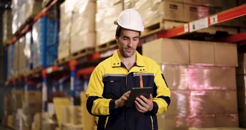 Warehouse worker in hardhat and safety jacket checks inventory data using 스톡 동영상 329460725