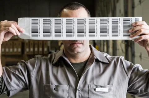 A warehouse worker holding up a sheet of bar code shipping lables in a Stock Photos