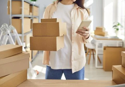 Warehouse worker holding stack of packages and using logistic app on mobile Stock-Fotos