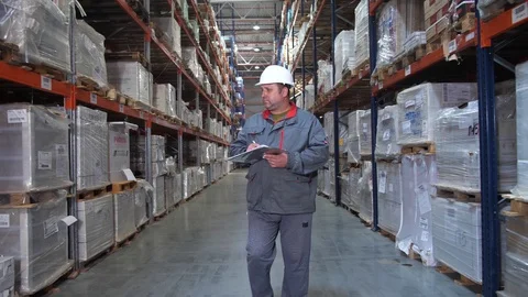 Warehouse worker inspecting high racks with boxes. A man walks in a row, the Stock Footage 111766492