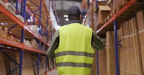 Warehouse worker inspecting shelves and stock in logistics aisle safety vest Stock Footage 335269859