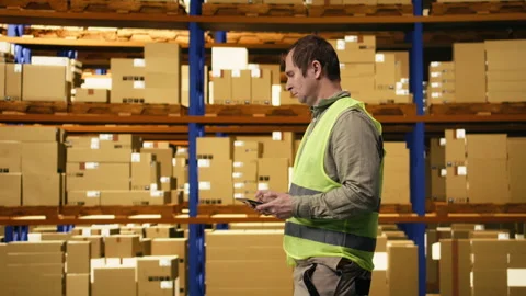 Warehouse worker overseeing pallets details on tablet in busy distribution hub Stock Footage 332908875