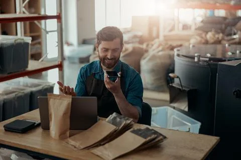 Warehouse worker record audio message on phone working on small coffee factory Stock Photos