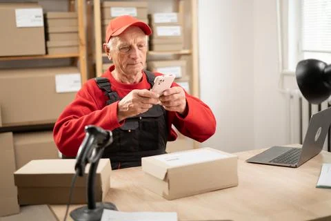 Warehouse worker in uniform using smartphone to scan barcode on parcel. Sma.. Stock Photos