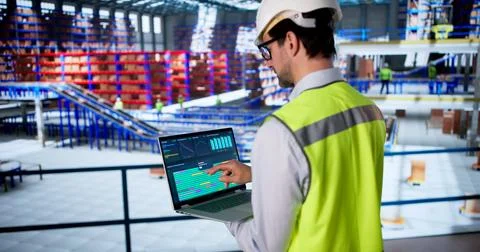 Warehouse Worker Uses Computer To Inspect Data And Monitor Safety. 库存照片