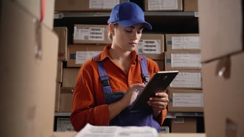Warehouse worker uses digital tablet for checking stock standing near shelves Stock Footage 249866935