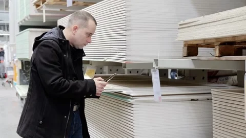 Warehouse worker verifying drywall inventory using smartphone, scanning pallet Stock Footage 328020769