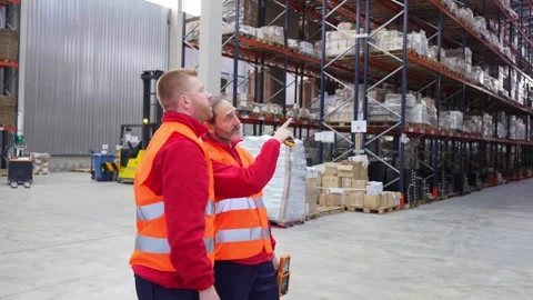 Warehouse workers discussing logistics and pointing at storage shelves Stock Footage 312856299
