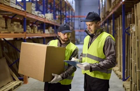 Warehouse workers doing inventory with clipboard and box in storage aisle Stock Photos