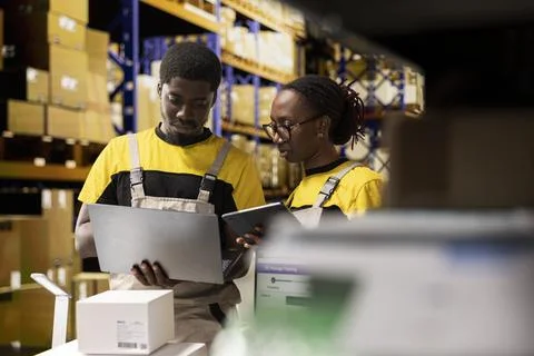 Warehouse workers overseeing parcels tracking info on laptop Stock Photos