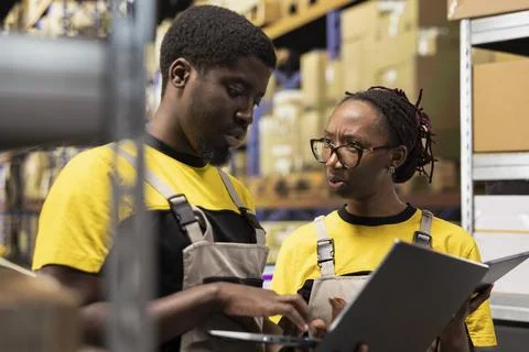 Warehouse workers overseeing parcels tracking info on laptop Stock Photos