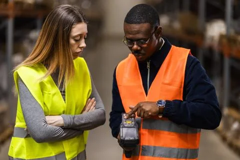Warehouse workers in reflective vests discussing scanning technology in an Stock Photos