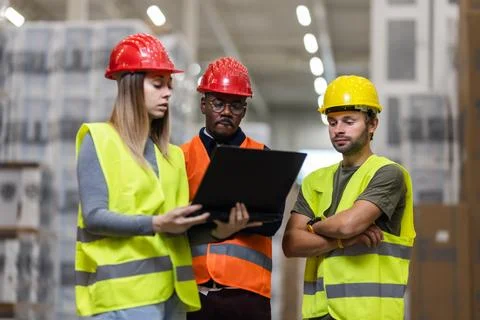 Warehouse workers reviewing project plans with a laptop in a storage facility Stock Photos
