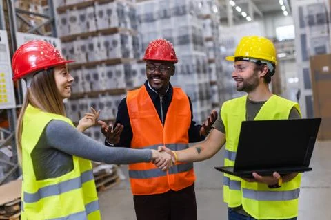 Warehouse workers in safety vests discussing and using a laptop in a factory Stock Photos