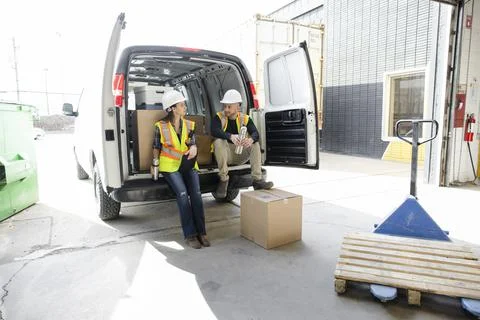 Warehouse workers taking coffee break at back of van at loading dock Stockfoto's