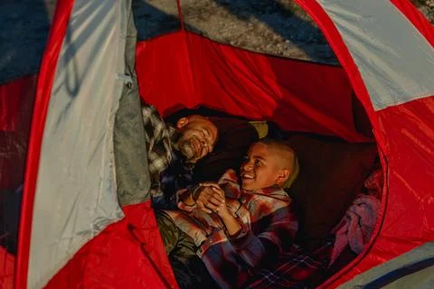 Warm and inviting image of dad and young son inside of a red camping tent Stock Photos