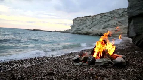 A warm bonfire burning on a rocky beach at dusk Stock-Footage 336399538