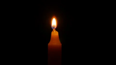 A warm candle flame burns steadily in open blackness while subtle flicker Stock Footage 323439079
