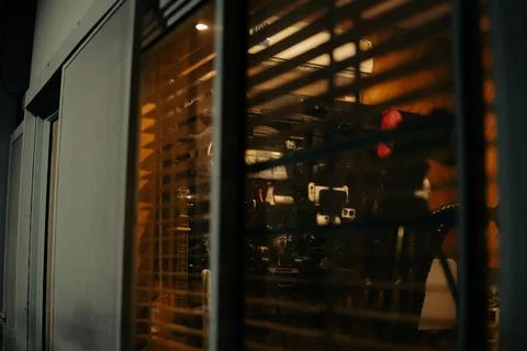 Warm Cinematic Desk Setup Viewed Through Window Blinds at Night Stock Photos