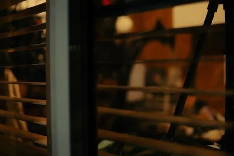 Warm Cinematic Desk Setup Viewed Through Window Blinds at Night Stock Photos