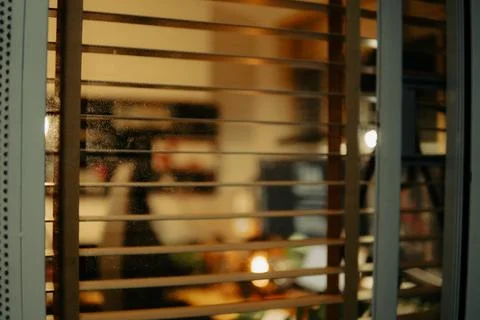 Warm Cinematic Desk Setup Viewed Through Window Blinds at Night Stock Photos