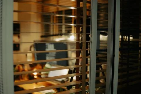 Warm Cinematic Desk Setup Viewed Through Window Blinds at Night Stock Photos
