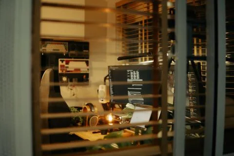 Warm Cinematic Desk Setup Viewed Through Window Blinds at Night Stock Photos