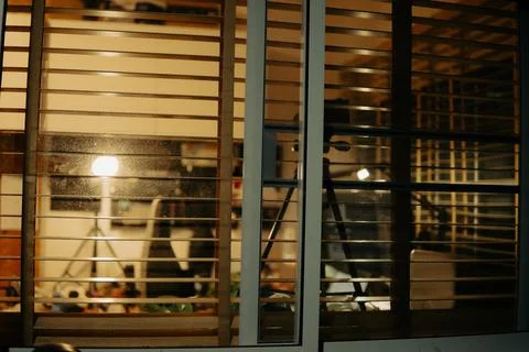 Warm Cinematic Desk Setup Viewed Through Window Blinds at Night Stock Photos