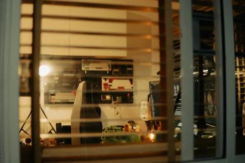 Warm Cinematic Desk Setup Viewed Through Window Blinds at Night Stock Photos