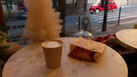 A Warm Coffee Cup and a Flaky Croissant Sitting Together on a Table with a Stock Footage 318496465