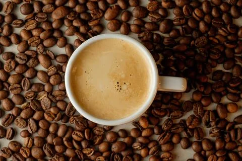 Warm coffee cup surrounded by roasted coffee beans on a rustic table Stock Photos