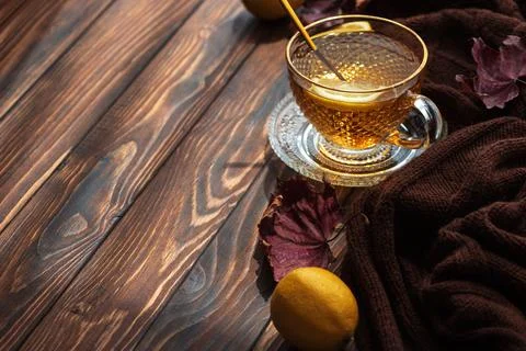 Warm cup of herbal tea with lemon slice and brown scarf on rustic wooden tabl Stock Photos