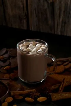 Warm drink with marshmallows surrounded by nuts and spices on wooden table Stock Photos