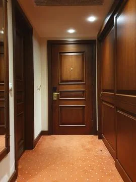 Warm, empty hotel hallway featuring a closed wooden room door, red dotted car 写真素材