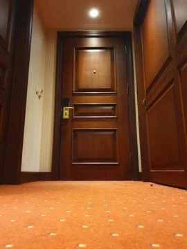Warm, empty hotel hallway featuring a closed wooden room door, red dotted car Фото