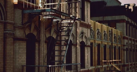 Warm evening light casts shadows on a fire escape attached to a brick building Stock Footage 319669042