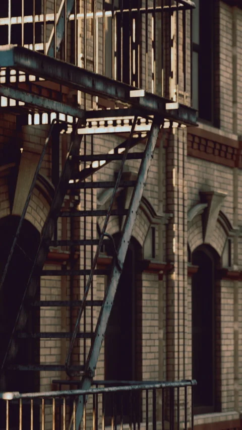 Warm evening light casts shadows on a fire escape attached to a brick building Stock Footage 327254095