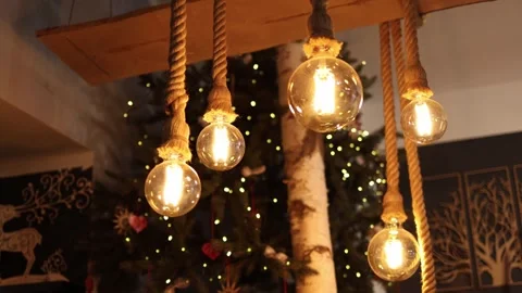 Warm glowing bulbs with rustic rope design shine against blurred Christmas tree  Video stock 317506478