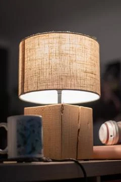 Warm glowing lamp with linen shade on wooden table in cosy interior Stock Photos