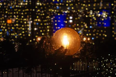 Warm glowing light bulb surrounded by Christmas garland with colorful bokeh.. Stock Photos