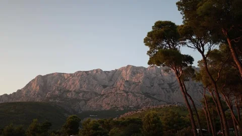 Warm golden hour sunlight illuminates rugged mountains above a peaceful pine for Stock Footage 341556809