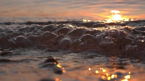 Warm golden sunset light illuminates bubbling ocean water along shore Stock Footage 337411050