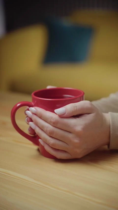 Warm hands cradle a bright red mug in a cozy indoor setting Stock Footage 303768162