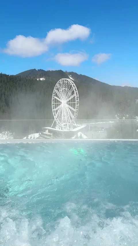 Warm infinity pool overlooking snowy mountains and ferris wheel Stock Footage 308824932