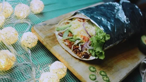Warm ingredient view: serving a foil-wrapped burrito on a rustic table Stock Footage 342168306