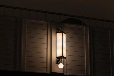 A warm interior wall lantern lamp casts a soft ambient glow across a modern.. Stock Photos