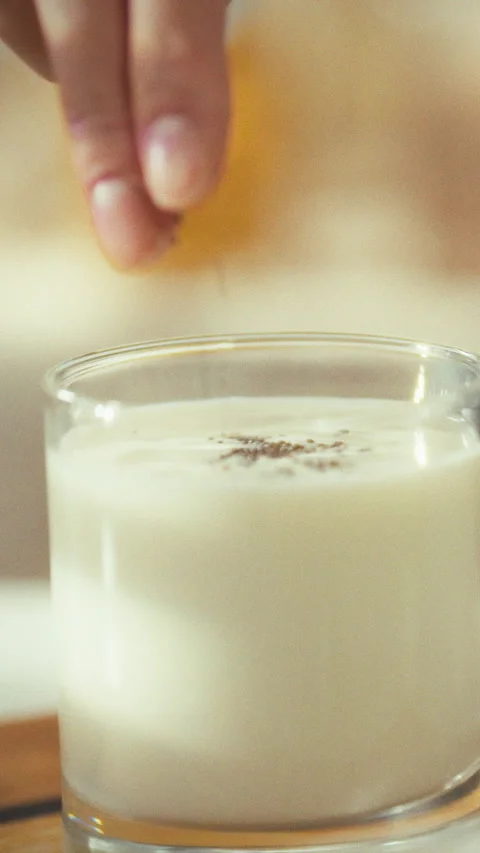 In warm kitchen person creatively enhances the flavor of glass of milk by ad Stock Footage 331795177