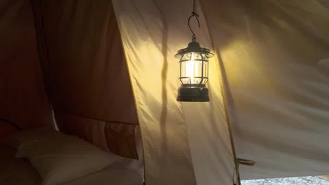 Warm LED camping lantern hanging inside a cozy canvas tent 库存影片 337977646